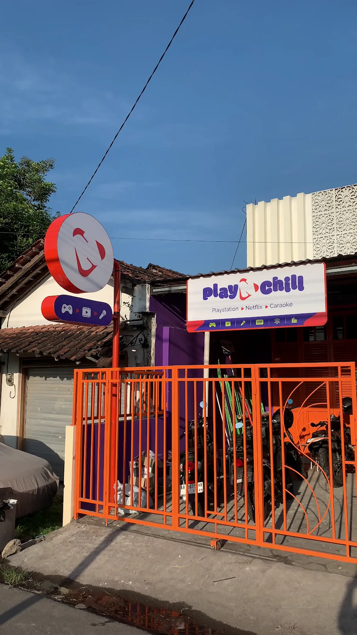Papan nama Play N Chill dan pagar oranye di tampak depan siang hari