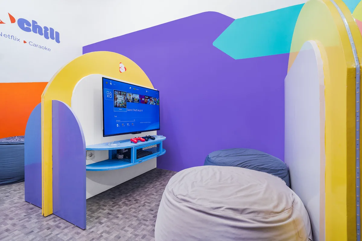 Bilik Play N Chill dengan dinding ungu, sekat melengkung, televisi dan bean bag